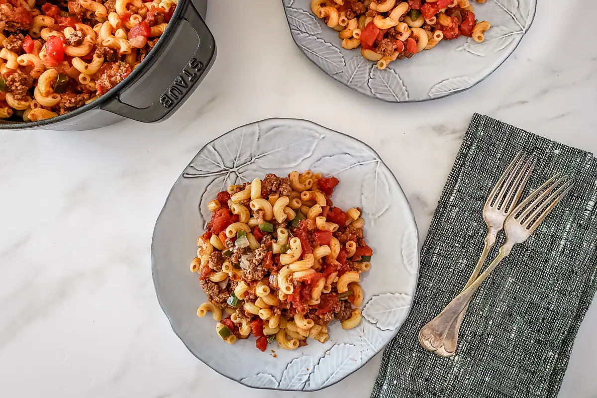 A plate of American chop suey with another plate and Dutch oven in the background.