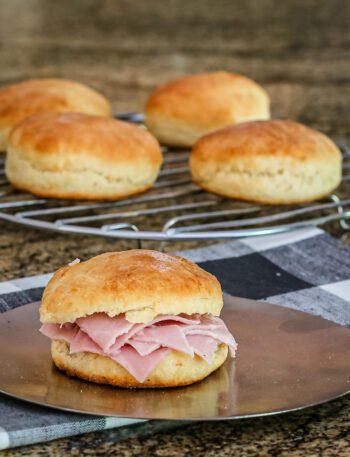 An angel cream biscuit with ham and some biscuits on a cooling rack in the background.