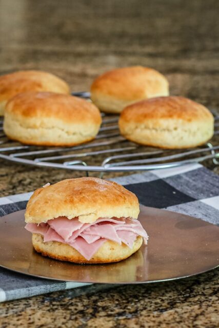 An angel cream biscuit with ham and some biscuits on a cooling rack in the background.