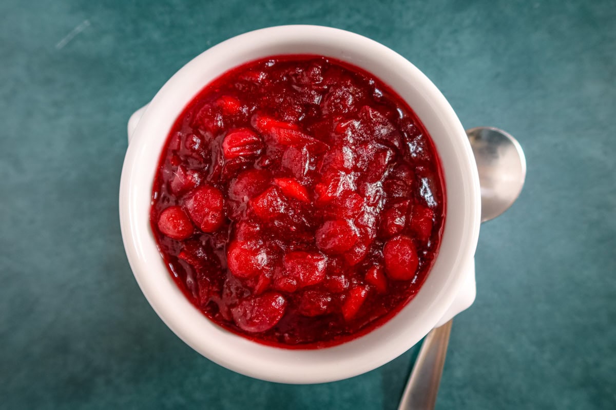 A serving bowl and spoon with freshly made apple cider cranberry sauce.