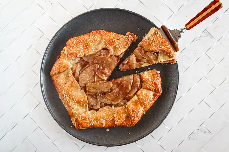 Fresh apple galette with sliced apples and flaky crust on a dark pie dish.