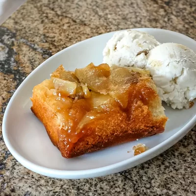 Golden apple cobbler with melting ice cream scoops on side.