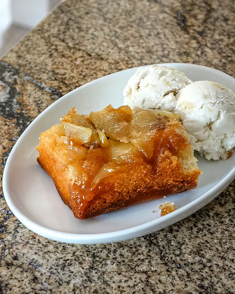 Golden apple cobbler with melting ice cream scoops on side.