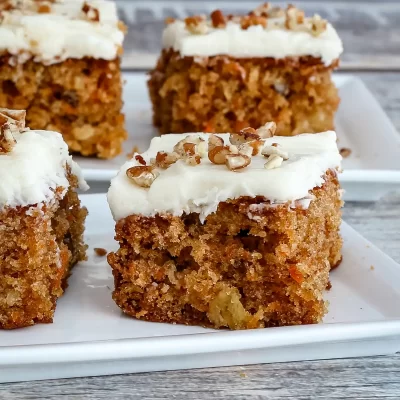 Moist carrot cake squares with cream cheese frosting and chopped nuts on top.