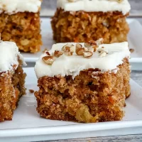 Soft carrot cake squares with cream cheese frosting and chopped nuts on top.