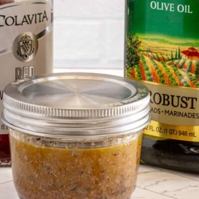 Freshly prepared seasoned meat mixture in a glass jar with olive oil and canned tomatoes in the background.