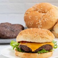 A juicy bacon cheeseburger on a sesame seed bun with lettuce and a slice of tomato.