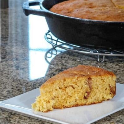 bacon and cheddar cornbread on a plate with the skillet in the background