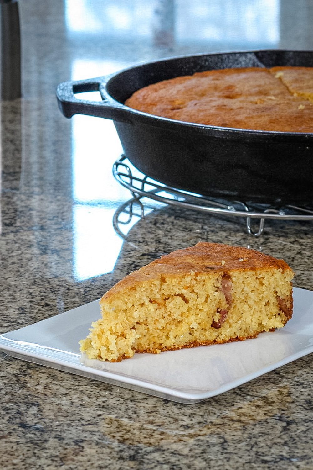 bacon and cheddar cornbread on a plate with the skillet in the background