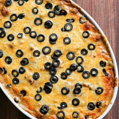 Freshly baked olive and cheese pizza in an oval dish on a wooden table.