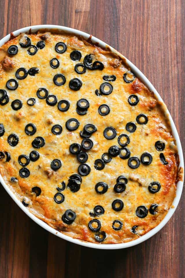 Freshly baked olive and cheese pizza in an oval dish on a wooden table.