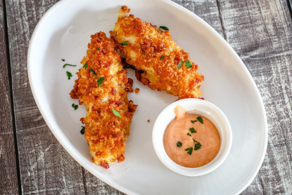 baked cheddar and bacon coated chicken strips with a small bowl of dip on the side.