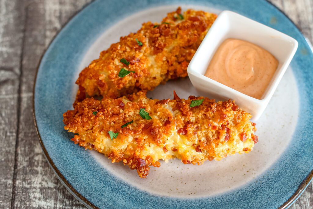 crispy baked cheddar and bacon coated chicken strips with a dip on the side.