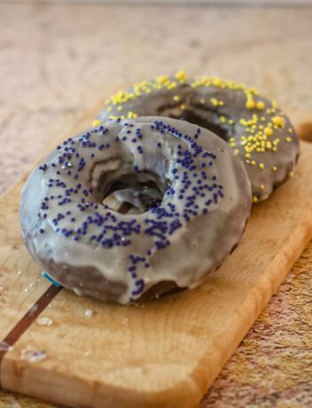 baked chocolate donuts with glaze and sprinkles on a small cutting board