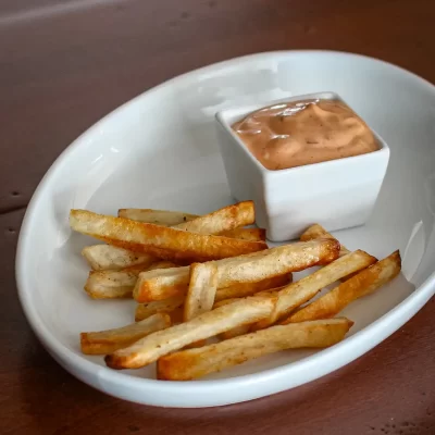 Crispy French fries with dipping sauce in a white bowl.