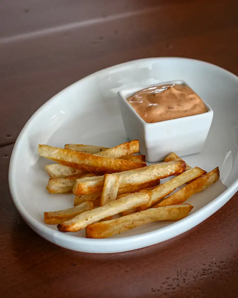 Crispy French fries with dipping sauce in a white bowl.