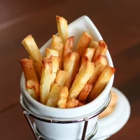 Golden crispy French fries in a white ceramic cup.