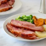 sliced baked ham on a plate with pineapple, sweet potatoes, and broccoli