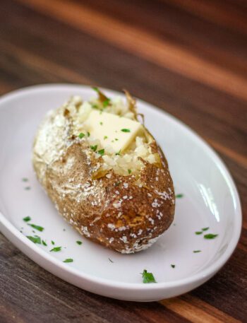 A baked potato on a plate with butter and parsley