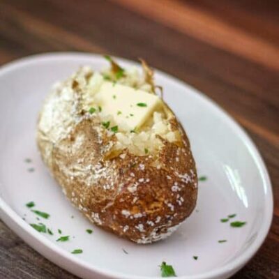 A baked potato on a plate with butter and parsley