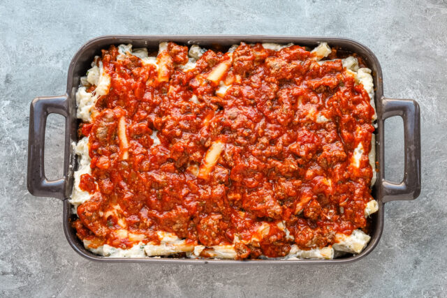 Layering the ziti mixture and meat sauce in the baking dish.