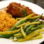 baked turkey legs with barbecue sauce, on a plate with rice and vegetables.