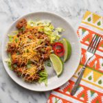 taco casserole on shredded lettuce with lime wedges