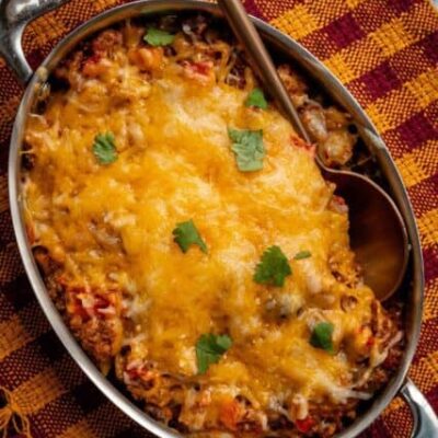 beef and bean taco casserole shown in a pan with melted cheese topping and cilantro leaves