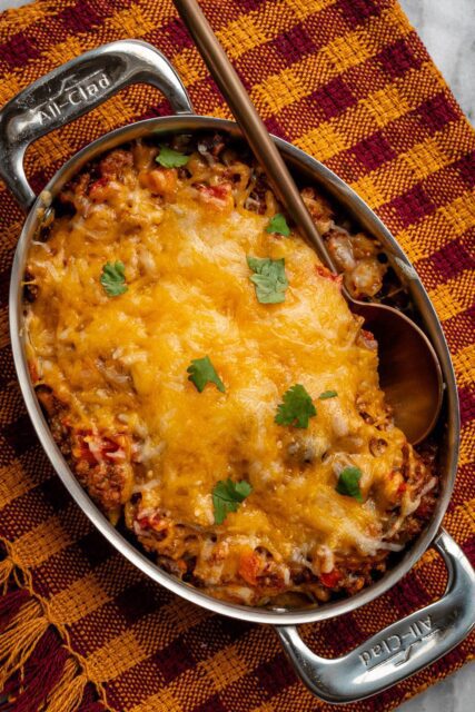 beef and bean taco casserole shown in a pan with melted cheese topping and cilantro leaves