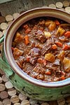 Hearty beef stew with vegetables and rich gravy in a green ceramic pot.
