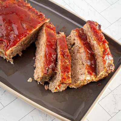 Ground meatloaf with tomato glaze on black tray.