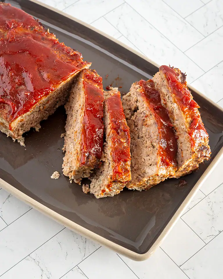 Ground meatloaf with tomato glaze on black tray.