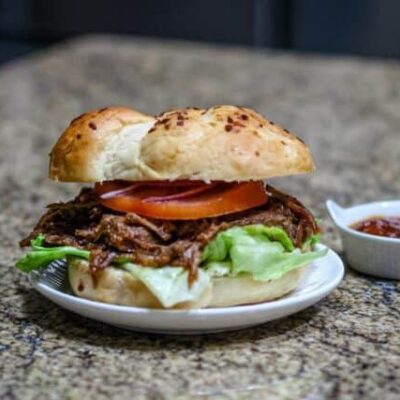barbecue beef sandwich on a small plate with barbecue sauce on the side.