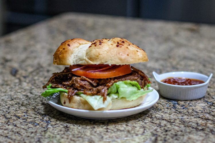 barbecue beef sandwich on a small plate with barbecue sauce on the side.