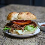 slow cooker barbecued beef shown in a toasted bun with lettuce and tomatoes