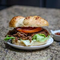 slow cooker barbecued beef shown in a toasted bun with lettuce and tomatoes