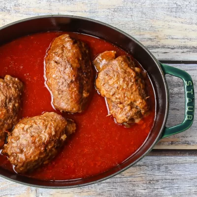Savory meatballs cooking in tomato sauce in a black skillet over a rustic wooden surface.