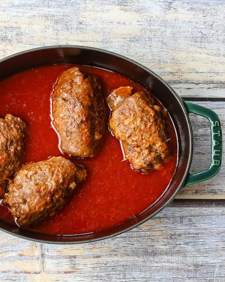 Savory meatballs cooking in tomato sauce in a black skillet over a rustic wooden surface.