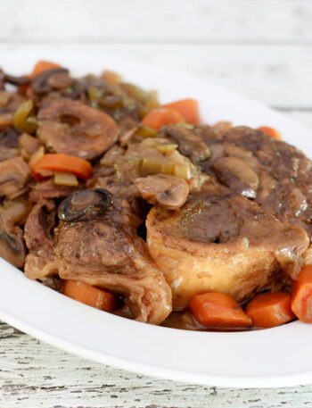 braised beef shanks on a platter with garlic, mushrooms, and carrots