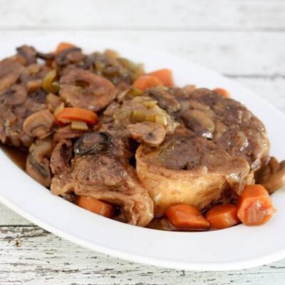braised beef shanks on a platter with garlic, mushrooms, and carrots