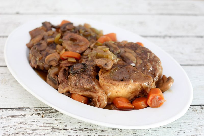braised beef shanks on a platter with garlic, mushrooms, and carrots