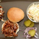beer braised pork shoulder is shown on a sandwich bun with slaw on the side.