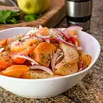 Sliced heirloom tomatoes with red onions and herbs in a white bowl.
