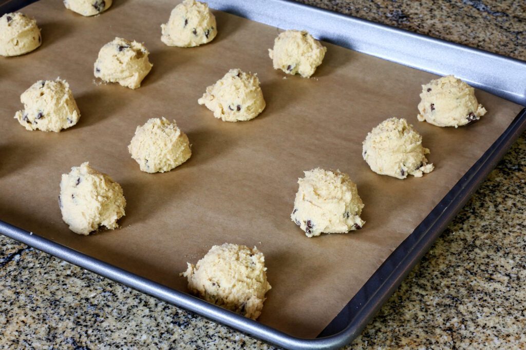 scoops of chocolate chip cookie dough on a parchment paper lined baking sheet.