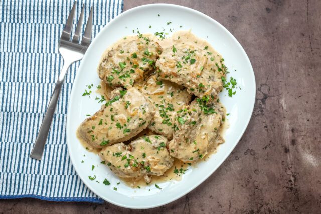 Smothered pork chops on a serving platter with parsley garnish.