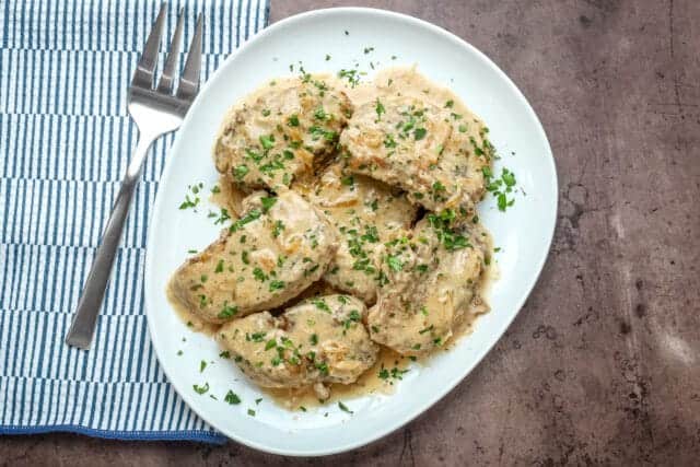 Creamy chicken with herbs on a white plate.