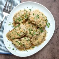 Creamy chicken breast with herbs on a white plate.