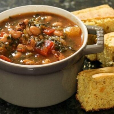 black-eyed pea soup with tomatoes and greens in a small cocotte with cornbread on the side