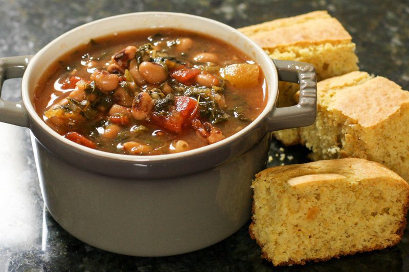 black-eyed pea soup with tomatoes and greens in a small cocotte with cornbread on the side