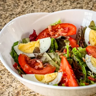 Fresh garden salad with tomatoes, boiled eggs, and bacon bits.